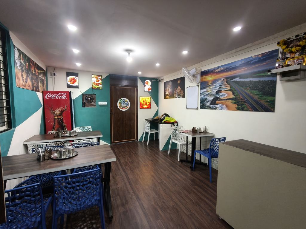 Dining room of Hotel Udupi Fish Corner with wooden tables, blue chairs, teal and white walls, and a large coastal landscape mural