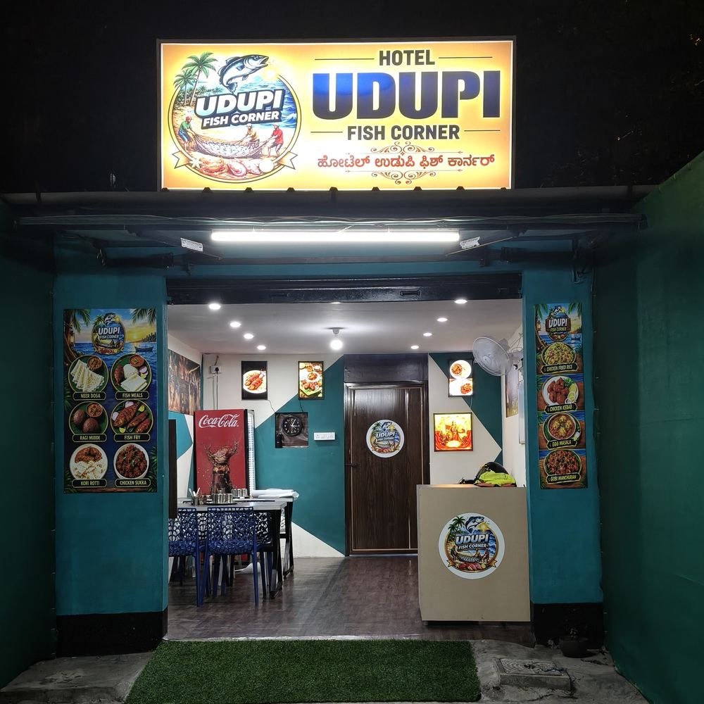 Entrance of Hotel Udupi Fish Corner at night, with its lit yellow sign above an open doorway and the dining room visible inside